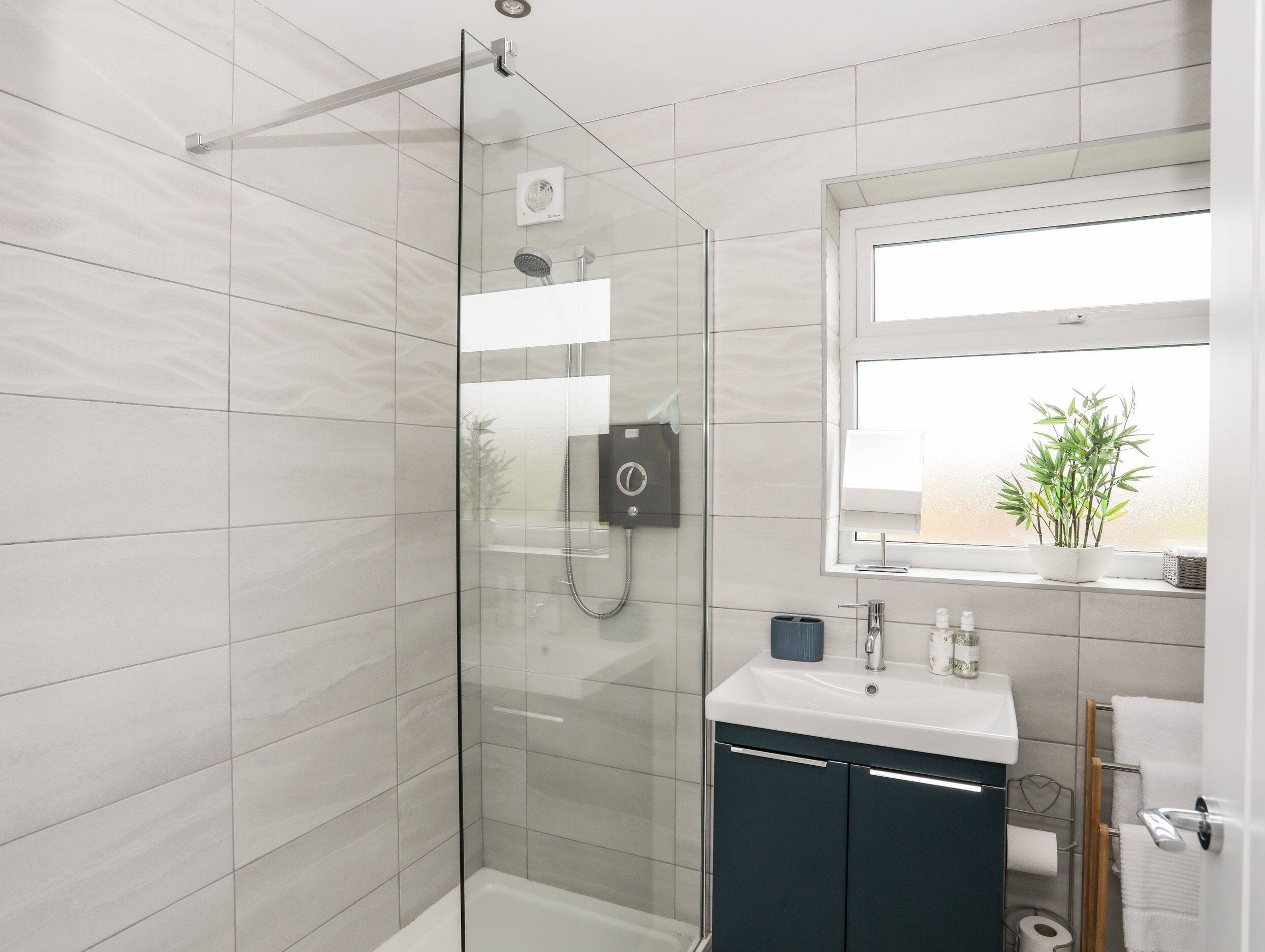 Une salle de bain moderne avec une douche à parois de verre, un lavabo blanc avec un miroir au-dessus, et une fenêtre donnant sur un paysage verdoyant.