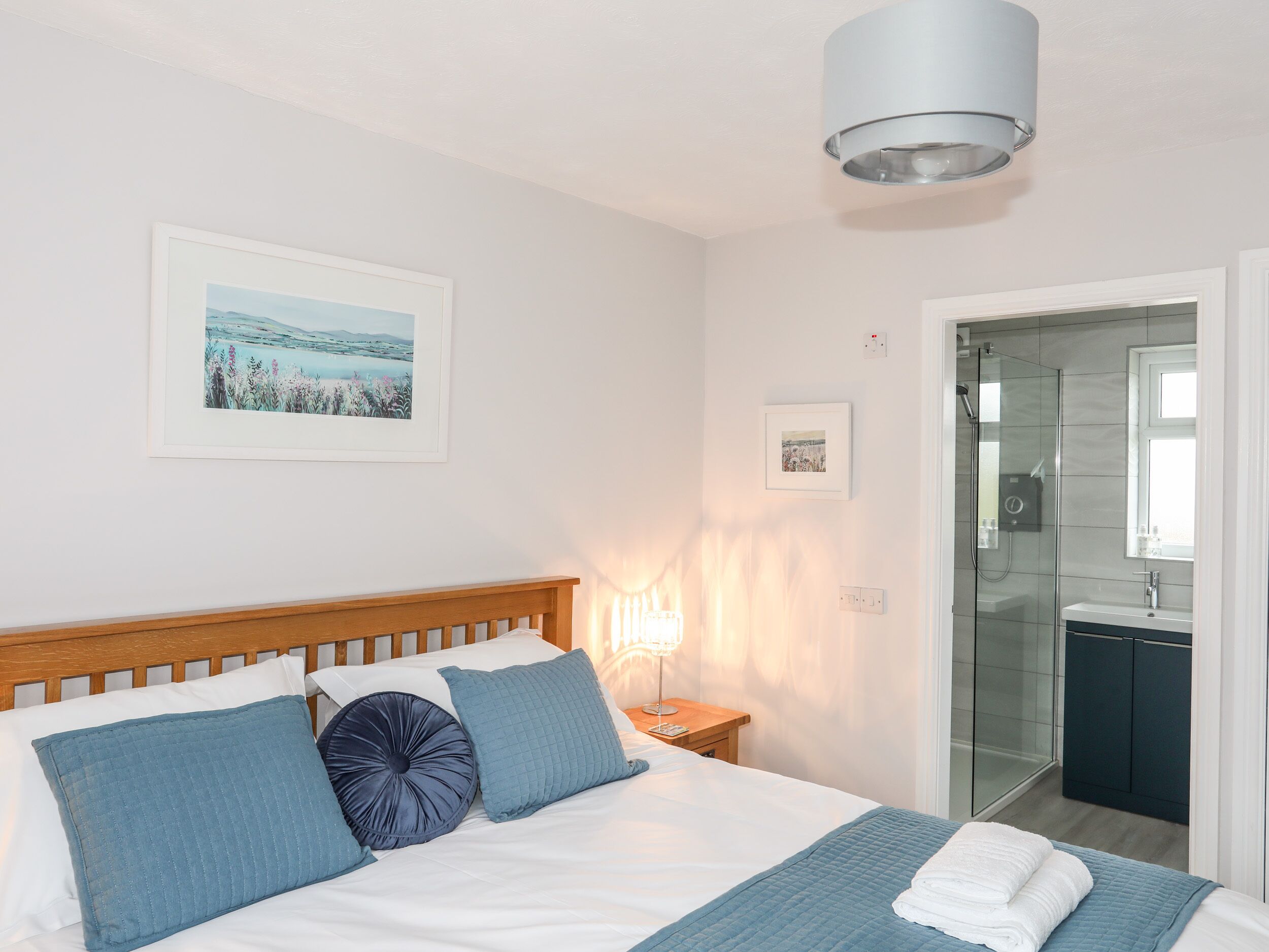 A neatly made bed with blue and white bedding, a bedside lamp, and framed pictures on the wall.