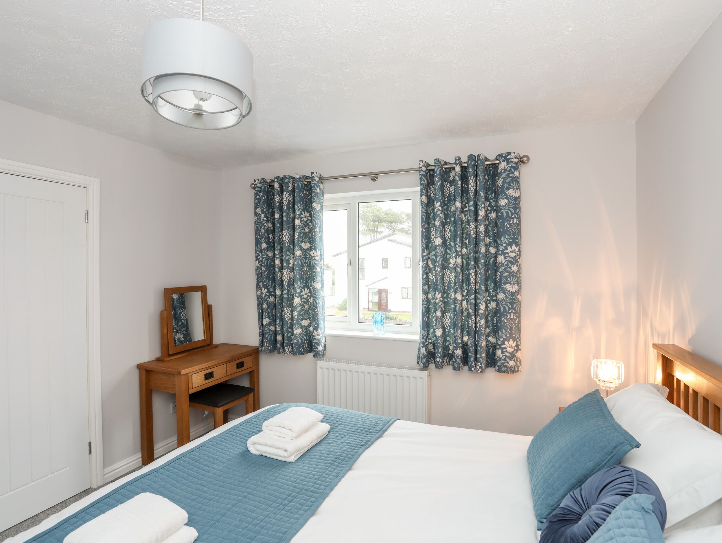 A bedroom with a bed, a bedside table, a mirror, and curtains.