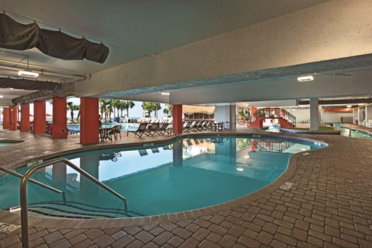 An indoor swimming pool with tiled flooring, red pillars, and lounge chairs.