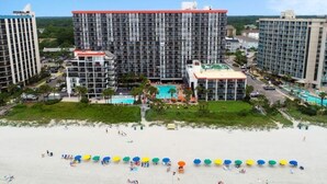 Un hôtel composé de plusieurs immeubles de grande hauteur, d’une plage aménagée avec des parasols et d’une piscine.