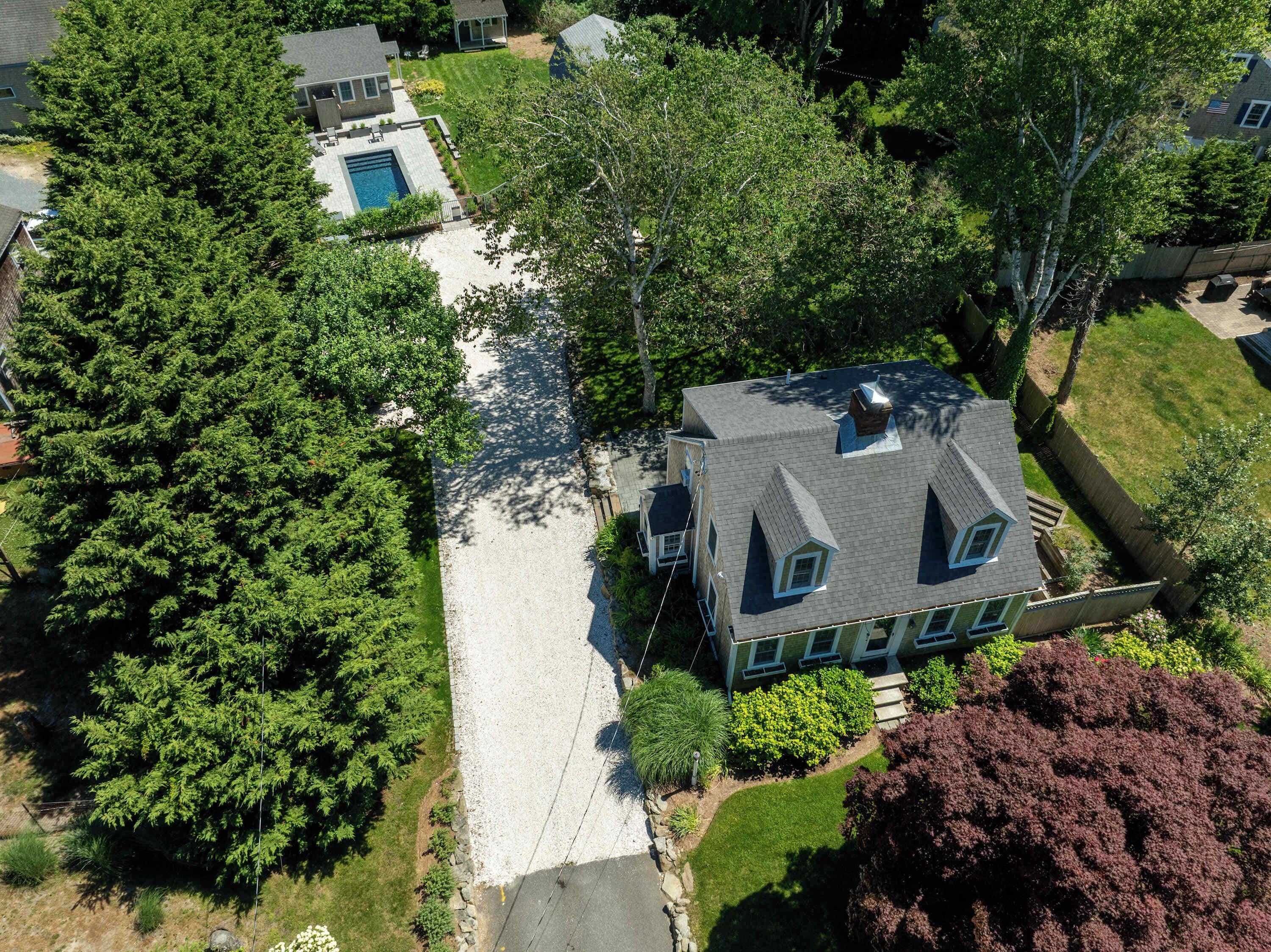 An aerial view of a residential property with a large house, a swimming pool, and surrounding greenery.