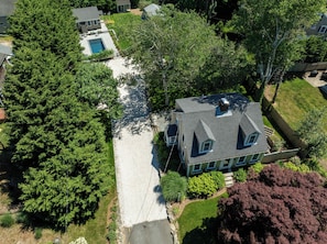 An aerial view of a residential property with a large house, a swimming pool, and surrounding greenery. - Heated Plunge Pool, Game Barn, AC, 5 Min to Beach! (Chatham)
