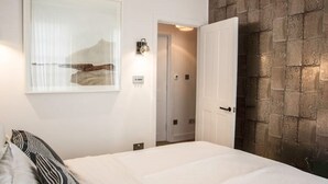 A bedroom with a bed, a wall-mounted light, a door, and a textured wall. - Stylish 2 Bedroom, 2 Bathroom Terraced Townhouse & Garden (LONDON)