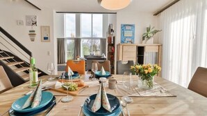 A dining area with a wooden table set for a meal, a staircase, and a view of the outdoors through large windows. - Villa Am Gutshof (Trent)