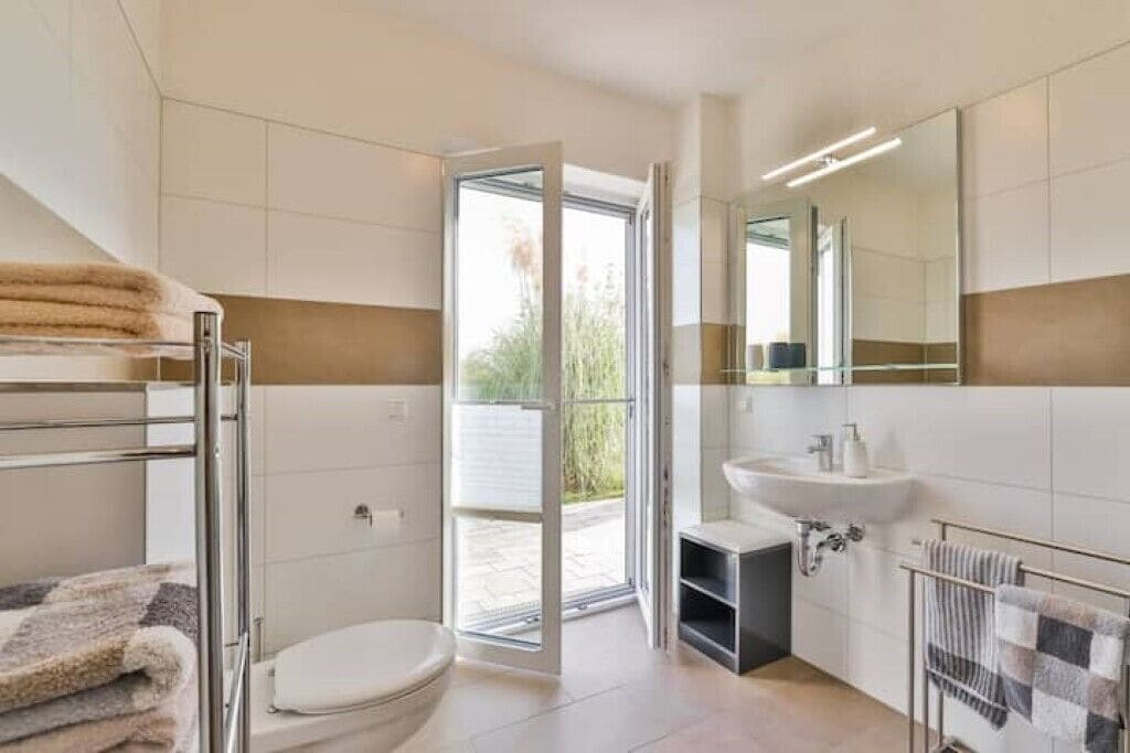 Een moderne badkamer met een douche, toilet en wastafel. Er is een glazen deur naar een buitenruimte.