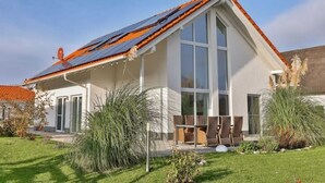A modern house with a sloped roof, large windows, and a patio area with outdoor furniture. - Villa Am Gutshof (Trent)