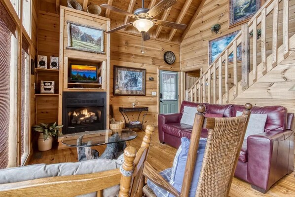 A cozy cabin interior with a fireplace, leather sofa, wooden walls, and a ceiling fan. - Abundant Views- Ultra-private and spacious cabin with abundant mountain views! (Sevierville)