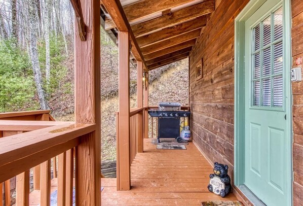 A wooden cabin with a porch, a grill, and a welcome sign.