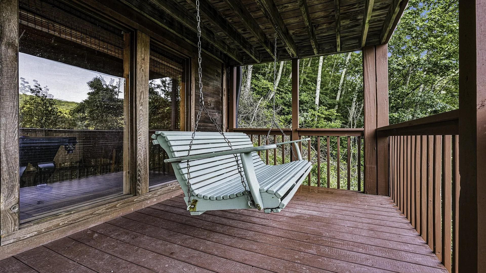 Une véranda en bois avec une chaise suspendue.