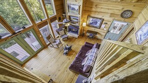 Interior de una cabaña con piso de madera, un sofá, una mesa de comedor, sillas, chimenea y ventilador de techo.