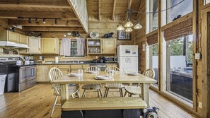 Cocina de cabaña de madera con una mesa de comedor para cuatro personas, armarios de madera, un refrigerador y un ventanal grande.