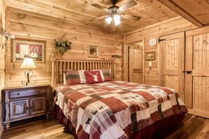 A cozy wooden bedroom with a bed, a nightstand, a lamp, a ceiling fan, and a door. - Abundant Views- Ultra-private and spacious cabin with abundant mountain views! (Sevierville)