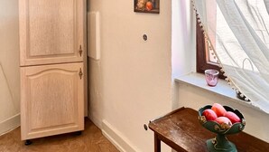 Una habitación con un armario de madera, una ventana con cortinas translúcidas y una mesita con frutero.