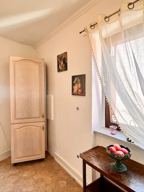Una habitación con un armario de madera, una ventana con cortinas translúcidas y una mesita con frutero.