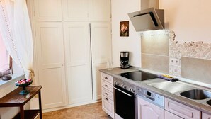 Una cocina compacta con armarios blancos, horno integrado, lavavajillas y cafetera.