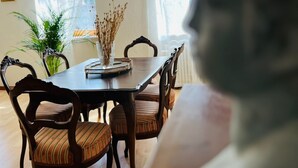 Un comedor con mesa y sillas de madera, un jarrón con plantas secas y una ventana con cortinas de gasa.