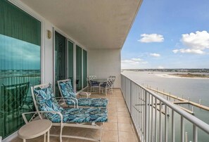 Ein Balkon mit zwei Lounge-Stühlen und einem Tisch, mit Blick auf ein Gewässer und eine entfernte Küstenlinie.