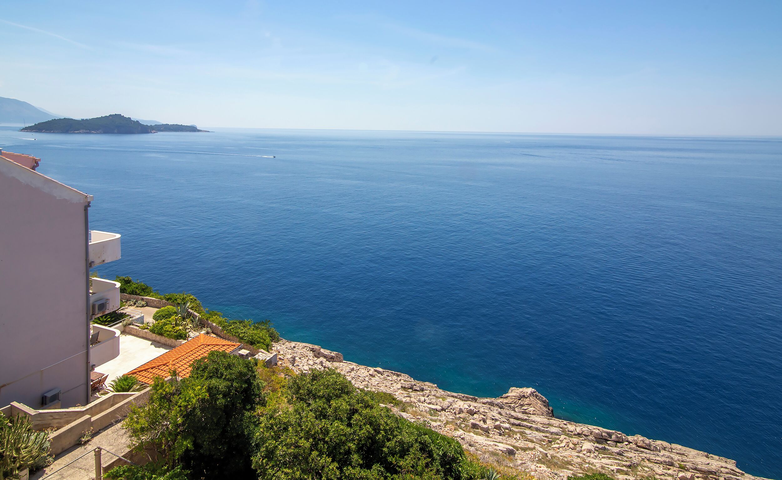 A coastal view with a building overlooking the sea, a rocky shoreline, and a distant island.