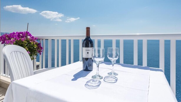 A table with a bottle of wine and two glasses on a balcony with a white railing and a view of the sea. - Kate`s place with balcony and amazing sea view for 3 persons (Dubrovnik)