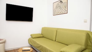 A living room with a green sofa, a flat-screen TV, a framed artwork, and a small round table with a remote control. - Kate`s place with balcony and amazing sea view for 3 persons (Dubrovnik)