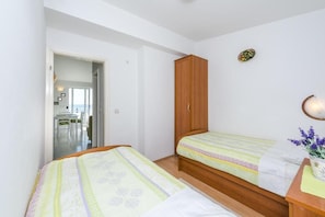Une chambre avec deux lits, une armoire en bois et une petite table sur laquelle est posée une plante.