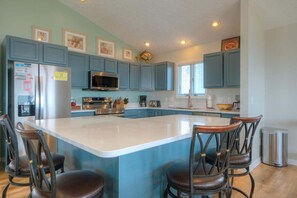 A kitchen with blue cabinets, a large island with bar stools, stainless steel appliances, and framed artwork on the walls.