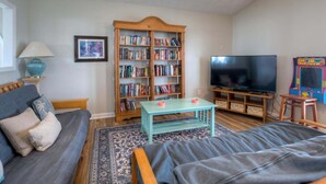 Un salon comprenant un canapé, une table basse, une bibliothèque, un téléviseur et une borne d’arcade pour enfants.