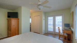 Une chambre à coucher comprenant un lit, une armoire en bois, un ventilateur de plafond et un bureau avec une chaise.