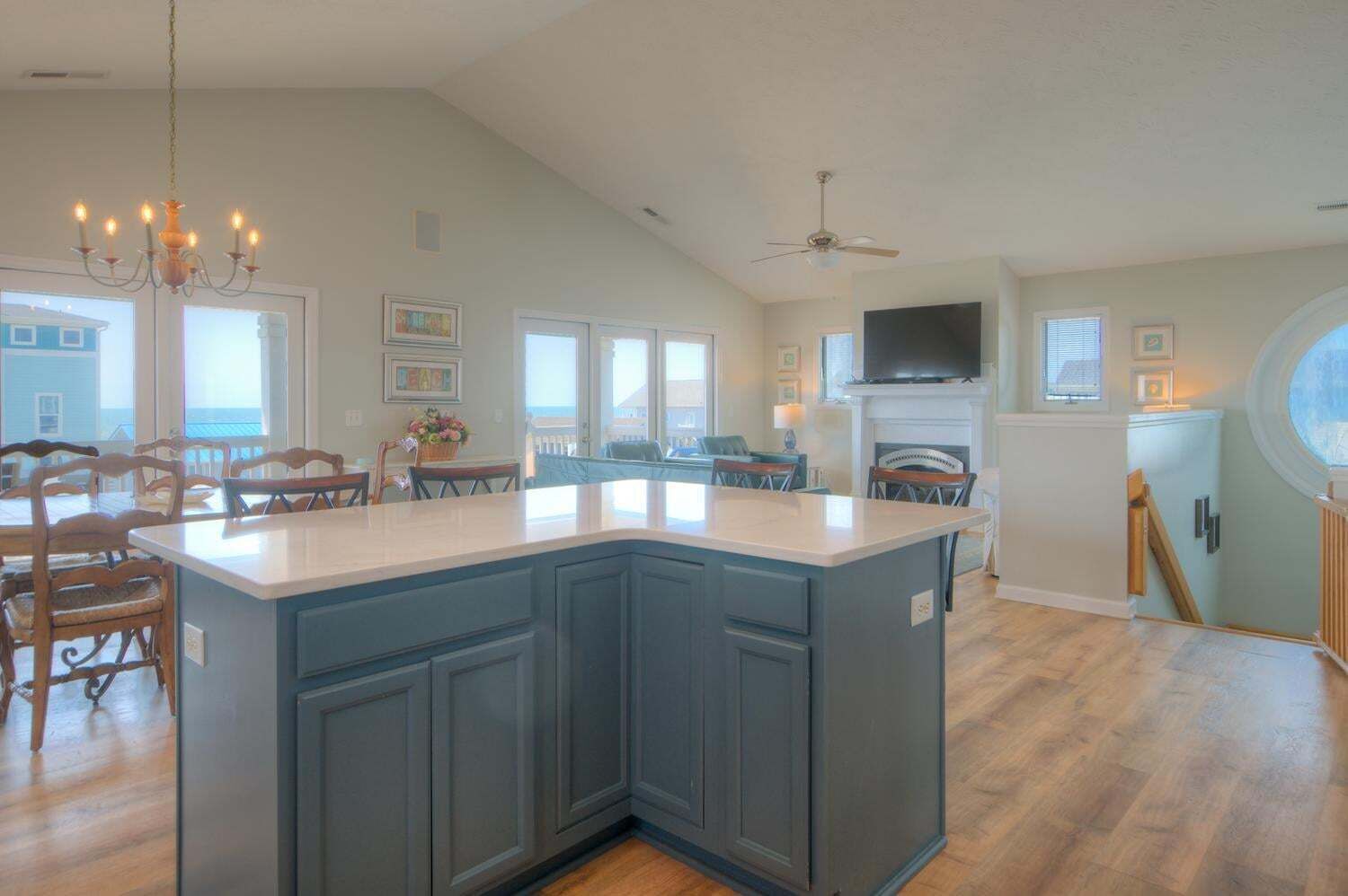 A kitchen with a large island, wooden chairs, a chandelier, and a ceiling fan.