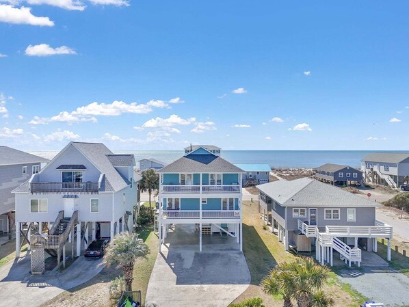 A beachfront property with multiple houses, including a two-story building with a balcony and a covered front porch. - Coral House: Spacious oceanview retreat in Oak Island, NC, perfect for families. (Oak Island)