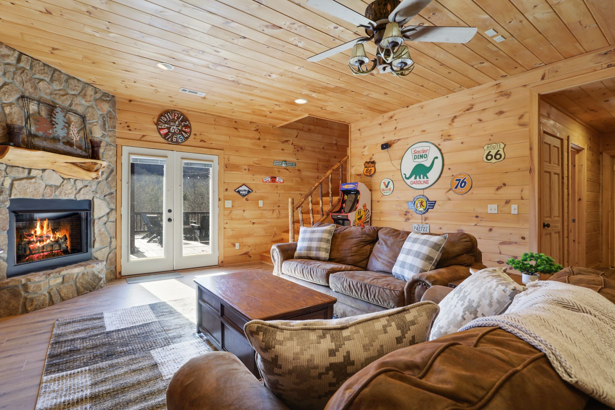 A cozy cabin interior with a stone fireplace, wooden walls, a ceiling fan, and various road signs.