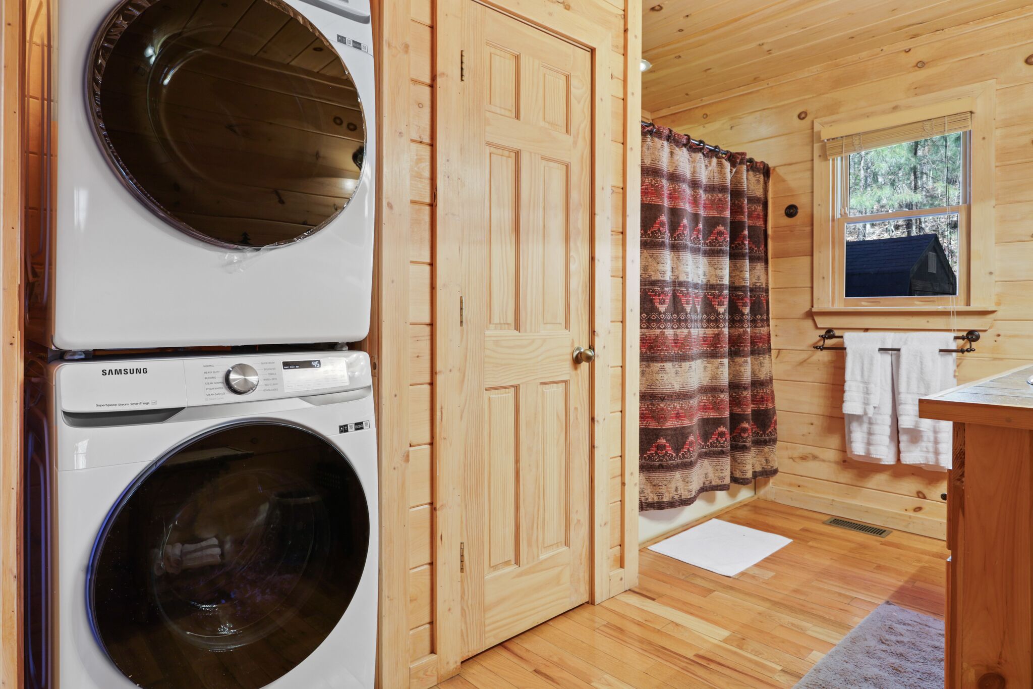 A laundry area with two washing machines, a wooden door, and a window with a view of trees.