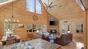 Une cabane en bois spacieuse, dotée d’une cheminée en pierre, de meubles en cuir et d’un grand téléviseur.