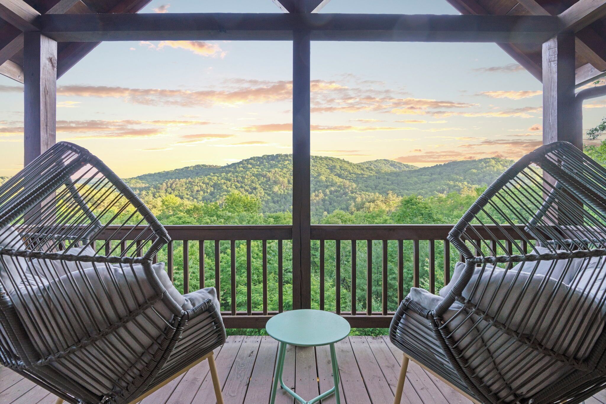 Área externa coberta com duas cadeiras de vime e uma pequena mesa, com vista para uma encosta arborizada.