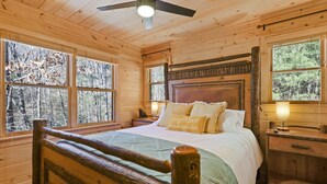 Une chambre dans une cabane en bois, avec un lit, des tables de chevet et un ventilateur de plafond.