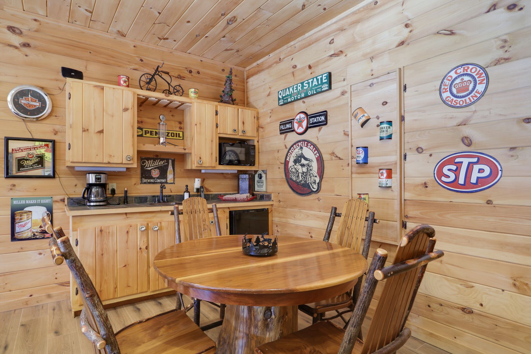 A wooden cabin interior with a dining table, chairs, a coffee maker, and various wall decorations including signs and a clock.
