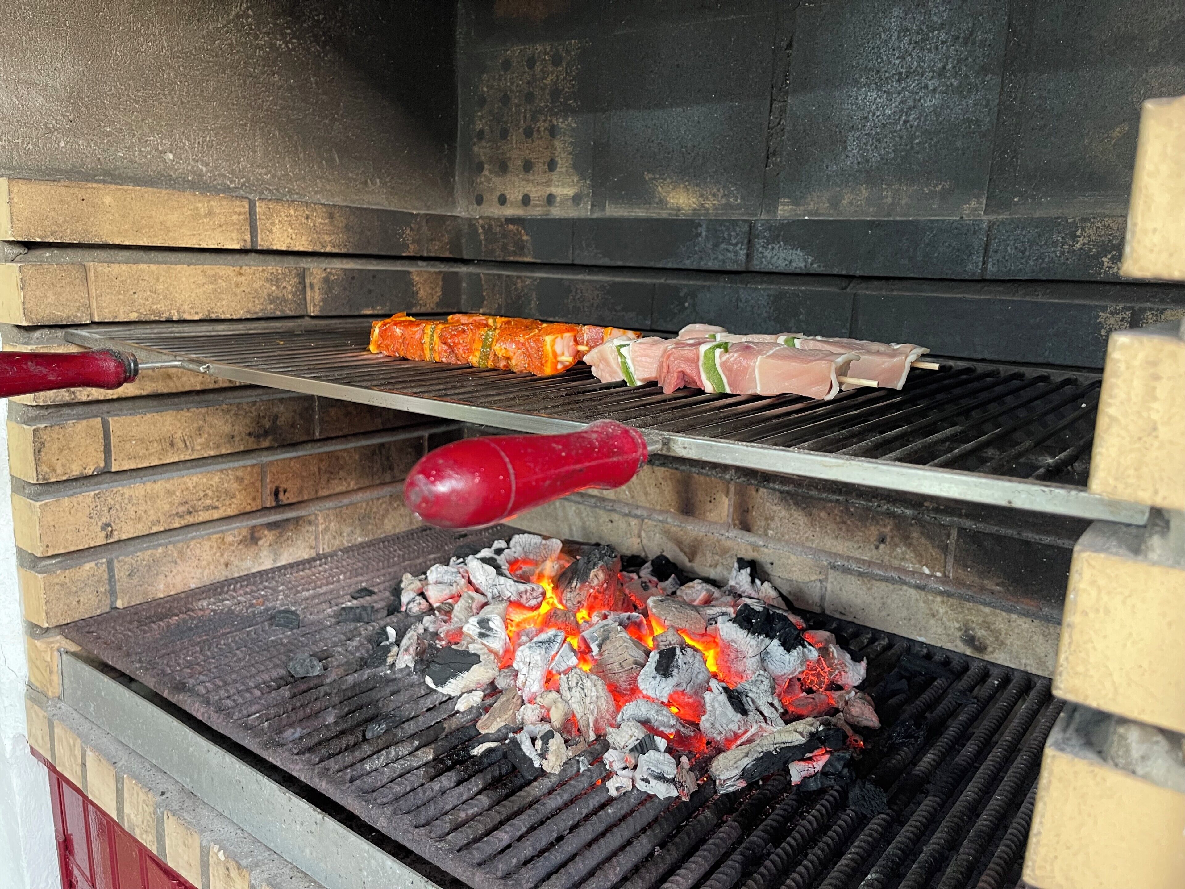 Una parrilla de carbón con brochetas de carne y verduras asándose.