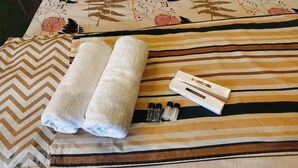 A bed with a striped pillow and two rolled towels. - Hotel Nirbana Heights (Dharamshala)