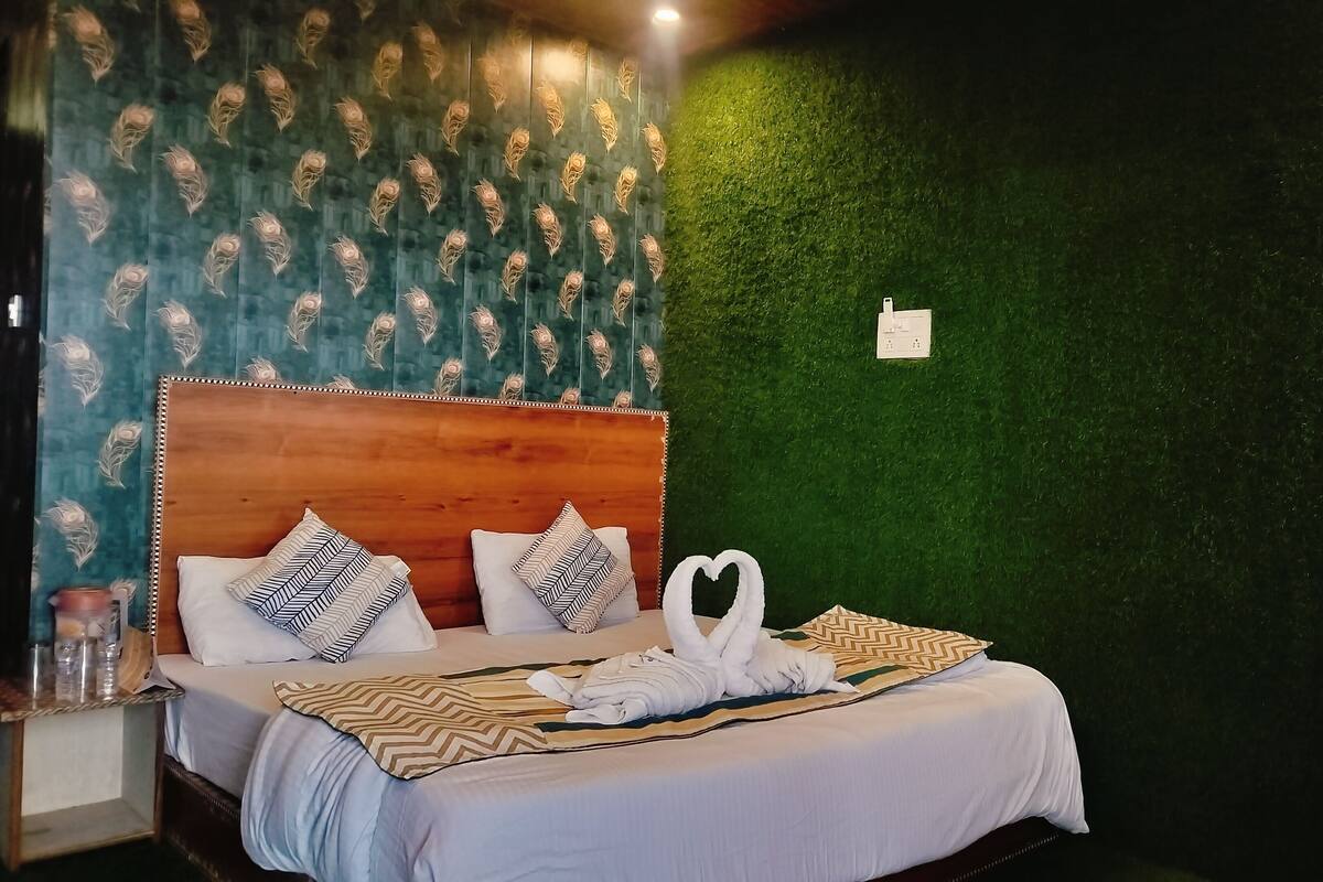 Una cama bien hecha con sábanas blancas y almohadones decorativos, un cabecero de madera y una pared verde con textura.