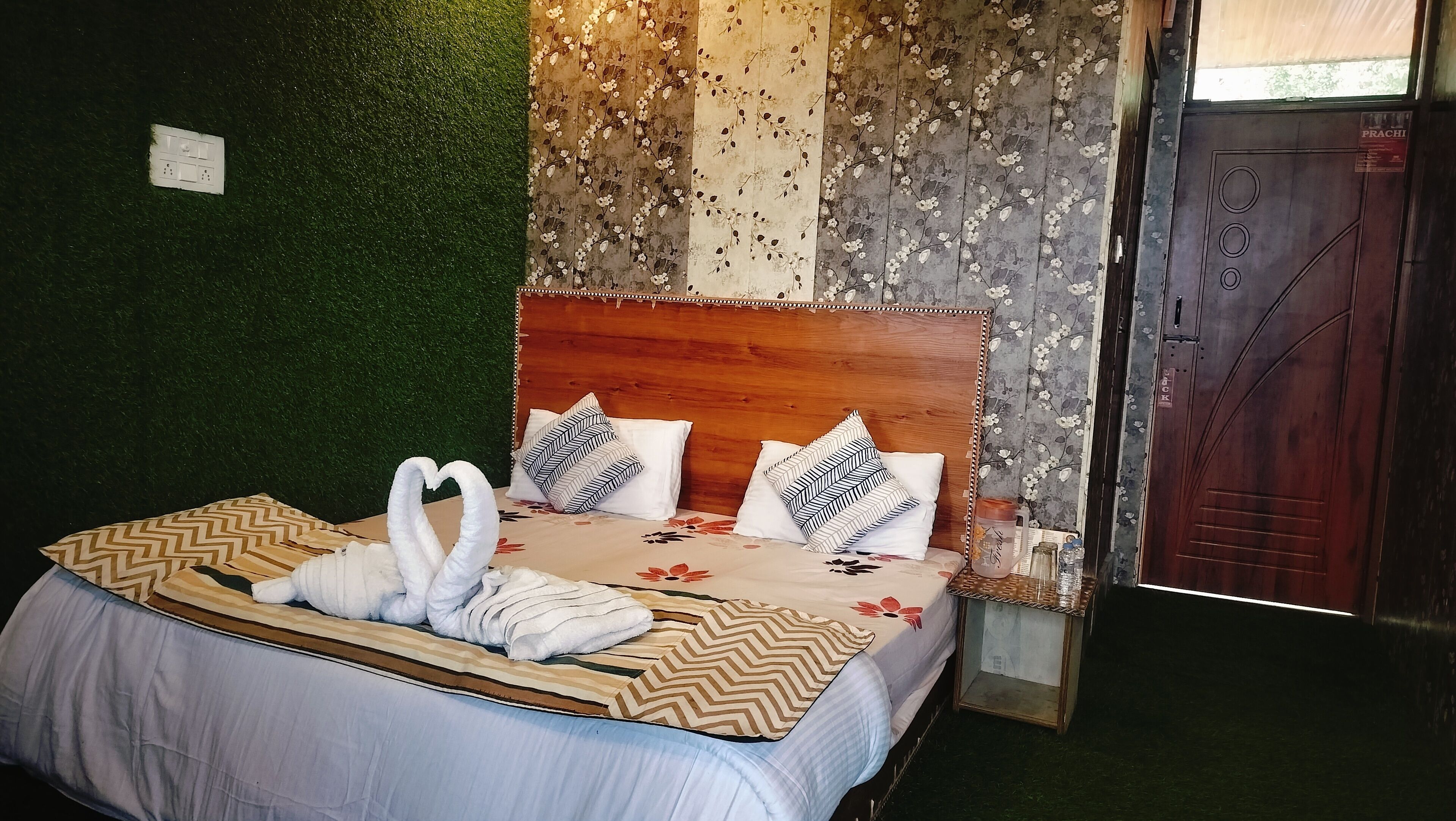 A neatly made bed with a floral bedspread, two pillows with a chevron pattern, and two towels arranged in a heart shape.