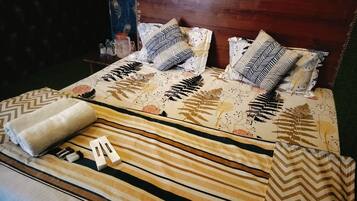 A neatly made bed with patterned bedding and pillows, a rolled-up towel, and a bedside table with a water bottle and salt shaker.