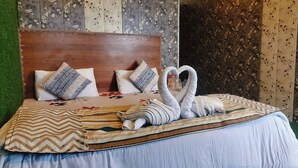 A neatly made bed with a wooden headboard, patterned pillows, and a decorative swan towel arrangement. - Hotel Nirbana Heights (Dharamshala)