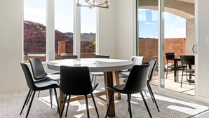 A modern dining area with a round table and black chairs, large windows, and a view of a brick wall and greenery outside. - Rainson Retreat 5 Bedroom Home (Washington)