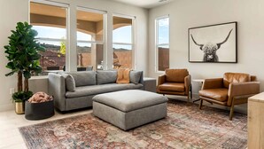 A living room with a gray sectional sofa, two leather armchairs, a patterned rug, and a large window offering a view of a brick wall and hills. - Rainson Retreat 5 Bedroom Home (Washington)