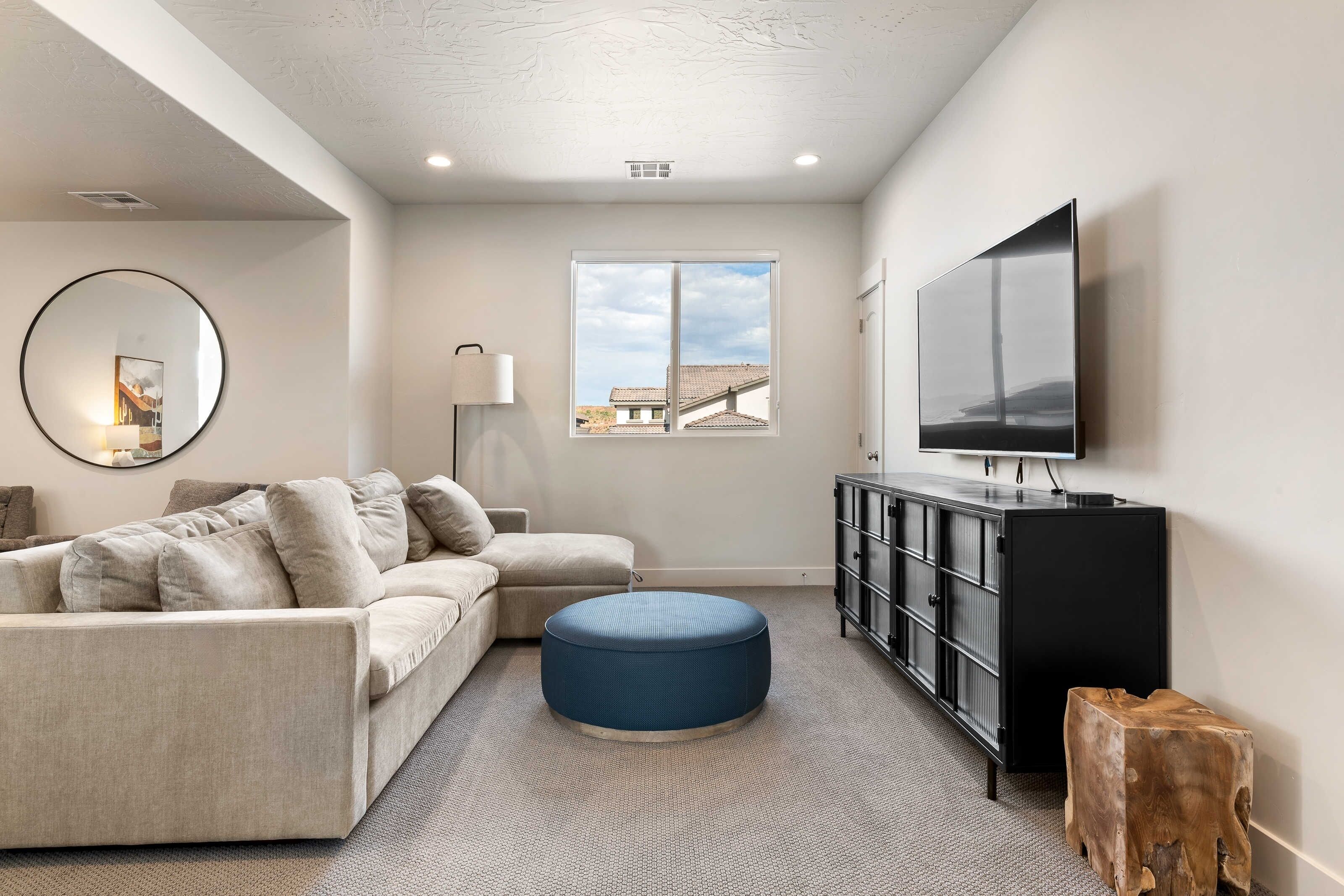 A modern living room with a sofa, ottoman, and a TV on a black cabinet.