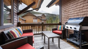 A covered outdoor patio with wicker furniture, a grill, and a view of a mountain cabin. - 45 Thackwell Lane 4 Bedroom Townhouse by RedAwning (Keystone)