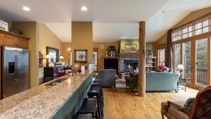 A spacious kitchen with a granite countertop and bar stools, a dining area with a fireplace, and a living room with a large window overlooking a deck. - 45 Thackwell Lane 4 Bedroom Townhouse by RedAwning (Keystone)