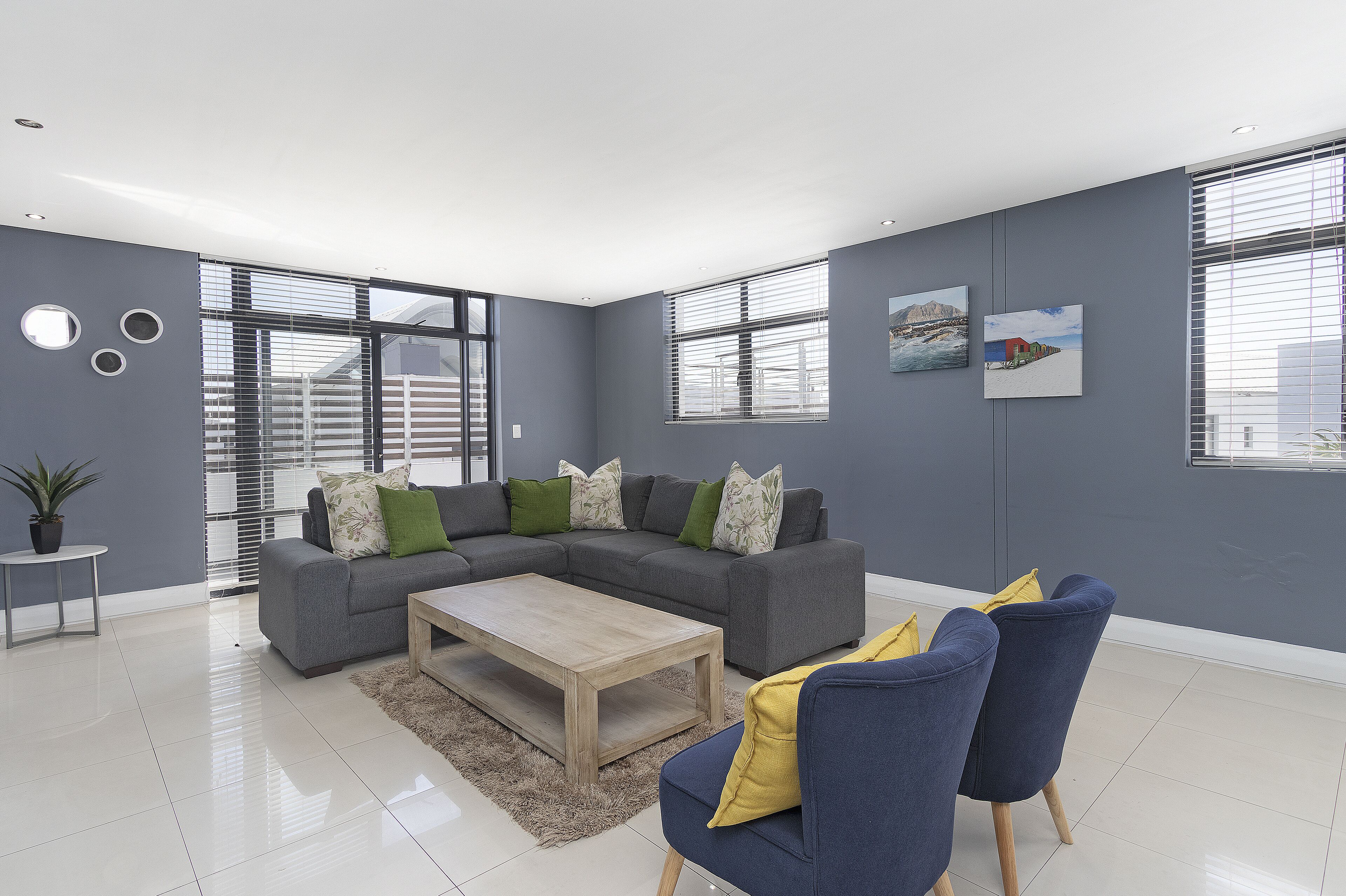 A modern living room with a grey sectional sofa, a wooden coffee table, and blue and yellow chairs.