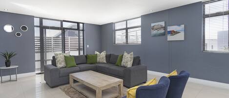 A modern living room with a grey sectional sofa, a wooden coffee table, and blue and yellow chairs.